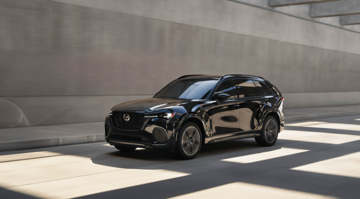 Black 2025 Mazda CX-70 SUV driving through a modern tunnel with sunlight casting shadows.
