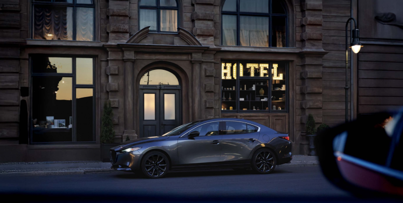 A gray 2026 Mazda3 sedan parked on a city street in front of a boutique hotel, highlighting its elegant and refined design at Middletown Mazda.