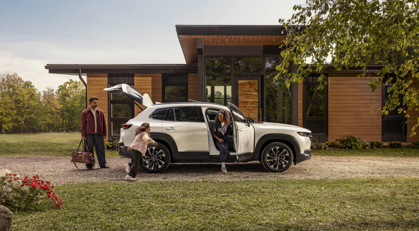 White 2026 Mazda CX-50 hybrid with family coming out to go into their home.